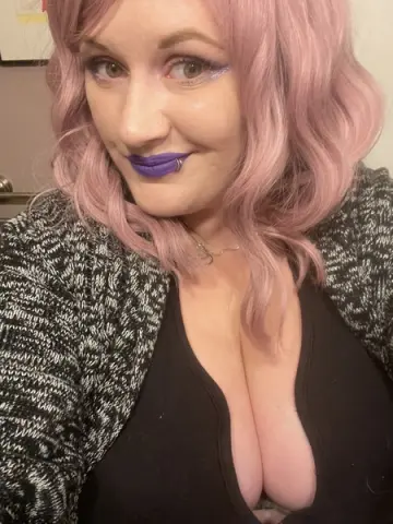 LuxieLuna smiles while wearing a black tank top and a grey knit cardigan with her pink hair styled in waves.