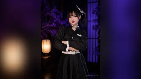 Young woman in black school uniform posing in a moody, purple-lit garden setting with lanterns.
