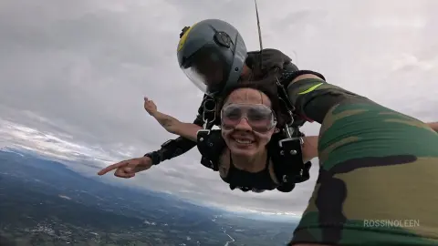 RossiNoleen skydives through a cloudy sky while wearing a black top and clear goggles.