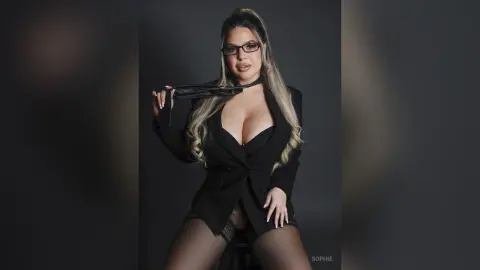 Confident woman in black blazer and glasses posing against a dark studio background.