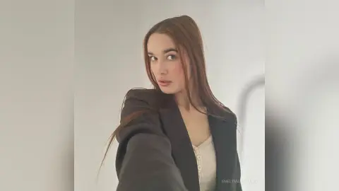 EmelyMastorovo poses in a black blazer over a white button-up top against a plain light background.