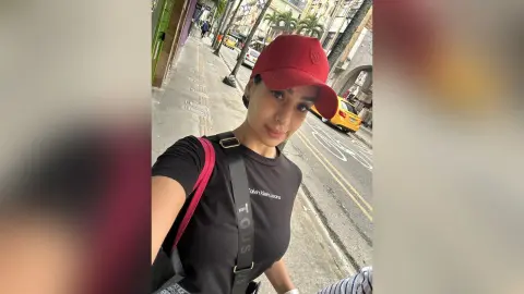Stylish woman in a black Calvin Klein t-shirt and red cap walking on a sunny city street.