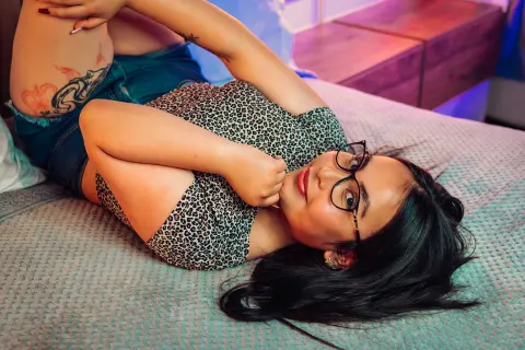 Smiling young woman in a leopard print top relaxing on a bed in cozy, warm indoor lighting.