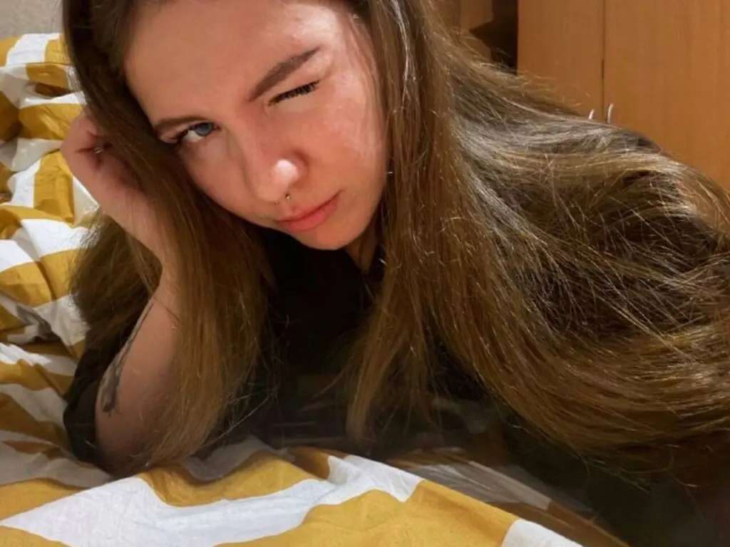 Young woman with long brown hair relaxing on a yellow patterned bed in a cozy indoor setting.