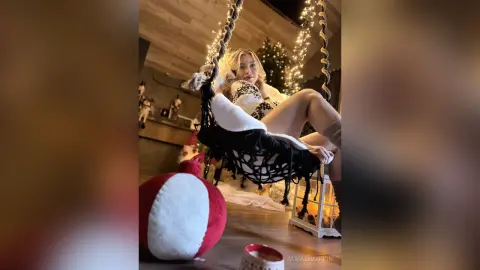 Young woman in a white patterned bikini relaxing on a hammock swing near a glowing Christmas tree.