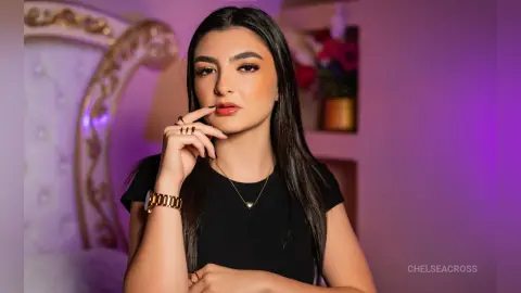 Young woman in a black t-shirt and gold necklace posing with a thoughtful expression in a soft purple room.
