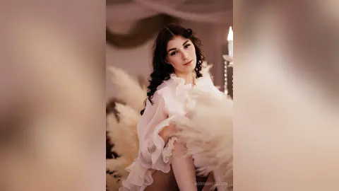 Elegant woman in a white ruffled gown posing in a dreamy, soft-lit romantic setting.