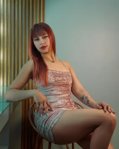 Redheaded woman in a pink velvet mini dress sitting in a modern room with a soft, elegant mood.