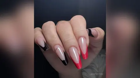 Elegant long coffin nails with a red and black ombre French tip design on a hand against a dark background.