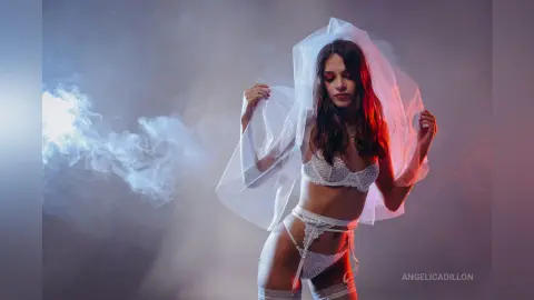 Young woman in white lace lingerie posing under a sheer veil amidst dreamy atmospheric smoke.