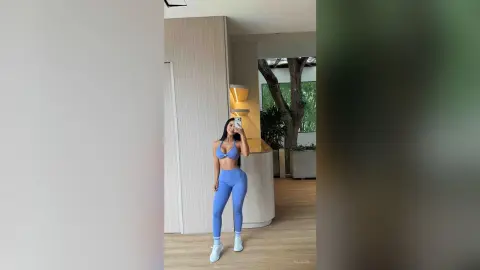 Alison poses in a blue bikini top and matching blue leggings while holding a phone for a mirror selfie.