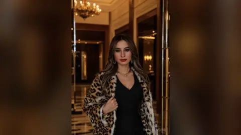 Elegant woman in a leopard print coat and black dress posing in a luxury hotel hallway.
