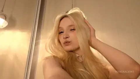 Blonde woman in a white top posing with a soft, dreamy expression in warm indoor lighting.