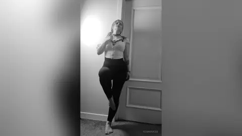 Moody black and white portrait of a woman in a white crop top and black leggings posing in a minimalist room.
