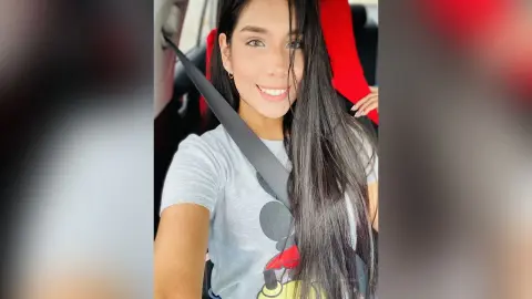 Smiling young woman with long dark hair wearing a grey graphic t-shirt in a car seat.