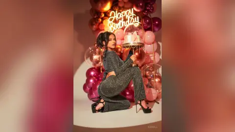Glamorous woman in a sparkly silver jumpsuit celebrating a birthday with a cake and pink balloons.