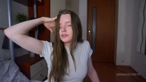 Young woman with long hair in a white t-shirt relaxing in a cozy bedroom setting.