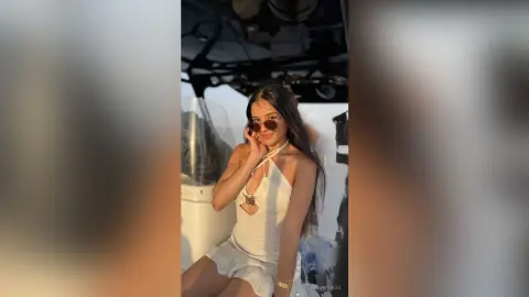 Young woman in a white halter dress and sunglasses posing in a bright, sunlit setting.