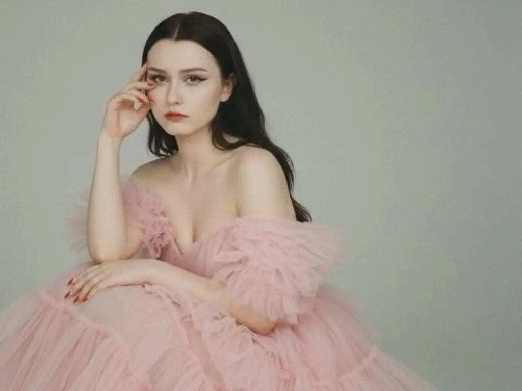Elegant woman in a voluminous pink tulle gown posing against a neutral background with a dreamy mood.