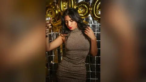 Glamorous woman in a sparkling gold cocktail dress holding a drink at a festive party with gold balloons.