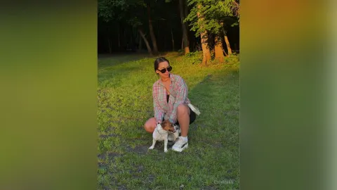 EmmyLee — EmmyLee sits in the grass wearing a plaid shirt and sunglasses while posing with a small dog.