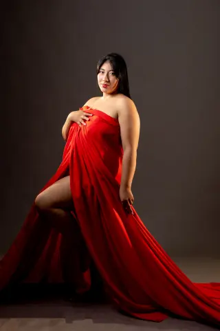 Elegant woman in a flowing red gown posing against a dark studio background for a dramatic portrait.