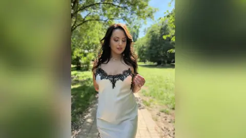 Elegant woman in a white lace slip dress walking through a sunny green park garden.