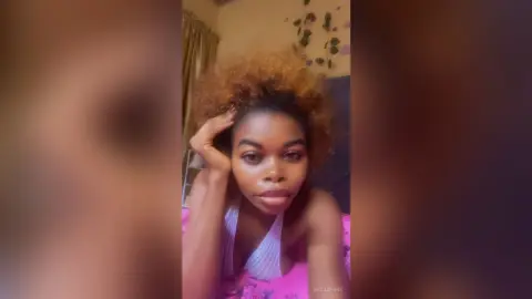 BecaSpark poses with her hand in her hair, wearing a white mesh top or bra.