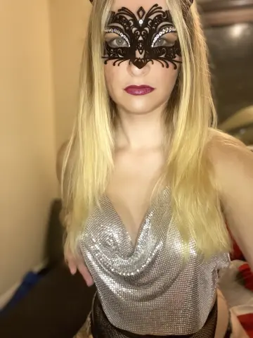 Blonde woman in a silver sequin dress and black lace masquerade mask posing for a glamorous evening look.
