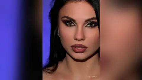 CutemEmma looks directly at the camera with long dark hair and heavy eye makeup, showing her face and shoulders against a blue background.