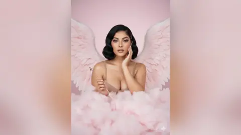 Elegant woman in a nude bodysuit with large white angel wings and a magic wand in a dreamy pink setting.