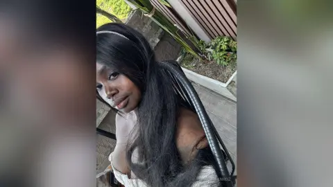 KeianHoz poses with long black hair and a thin headband, looking toward the camera in an outdoor setting.