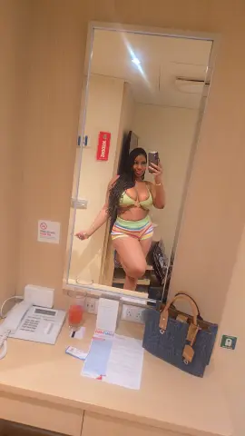 Curvy woman in a colorful striped bikini posing for a mirror selfie in a hotel room.