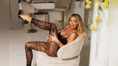 Glamorous woman in black lace lingerie and patterned fishnet tights relaxing in a modern white chair.