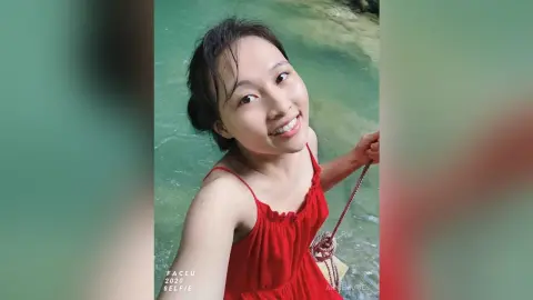 Smiling young woman in a red summer dress relaxing by a turquoise tropical lagoon.