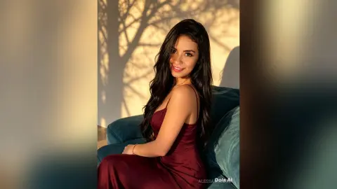 AlessaWaldorf sits on a teal couch wearing a red dress with her long dark hair flowing over her shoulder.