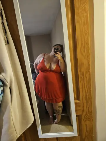 CurvesWithBBW poses for a mirror selfie wearing a short red dress that shows off her cleavage and legs.