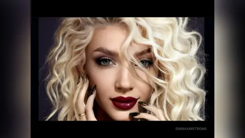 Glamorous blonde woman with wavy hair and dark red lipstick posing for a moody beauty portrait.