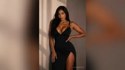 Elegant woman in a sleek black evening dress posing against a sunlit wall in a moody, sophisticated setting.