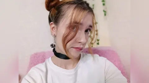 Young woman with reddish hair in a white t-shirt and black choker posing in a bright indoor setting.