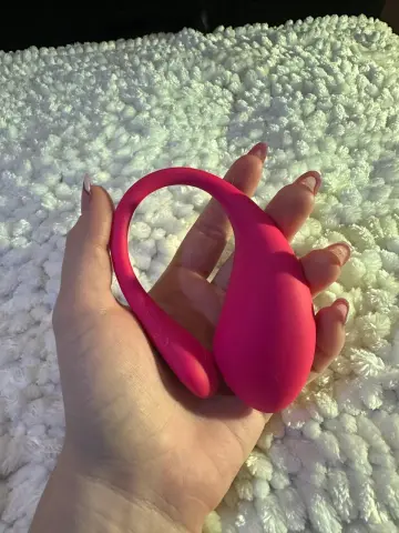 Hand holding a bright pink silicone massage tool against a white textured shag rug background.