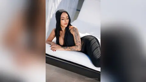 Stylish woman in black sleeveless top and leggings relaxing on a white lounge chair in bright sunlight.