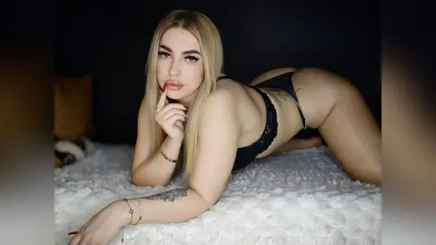 ZaraPlaya poses on all fours on a white bed, wearing a black lace bra and black thong, showing her bare back and buttocks.