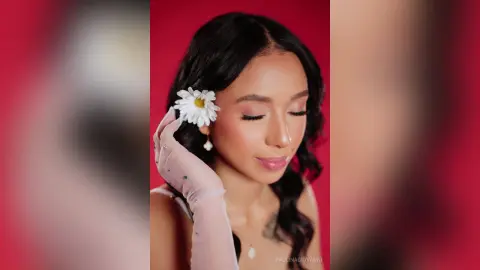 Beautiful woman with a white flower in her hair wearing sheer gloves against a romantic red background.