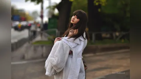 Stylish young woman in a white fuzzy coat and matching outfit posing on a city street with a soft, dreamy mood.