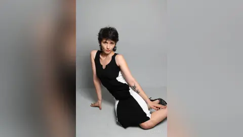IveteDurand poses in a black and white sleeveless dress, sitting on the floor with her hands resting on her legs and the ground.