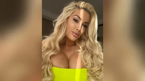Blonde woman in a bright yellow tube top smiling in a warm, sunlit indoor setting.