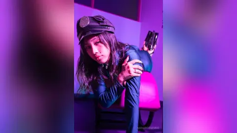 NashiroSakurai wears a black cap and a blue long-sleeved top while leaning forward over a pink chair.