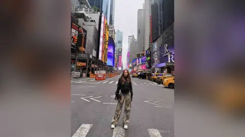 EvelynMills stands on a city street wearing a black long-sleeve top and patterned camouflage trousers.