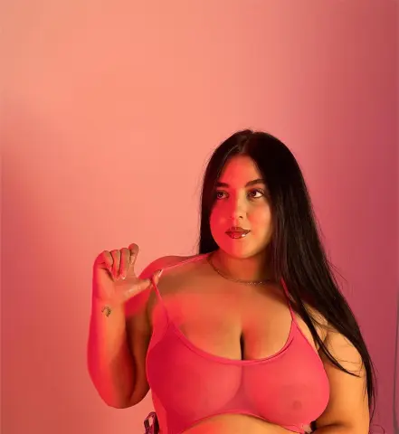 Young woman in pink lingerie posing against a warm pink background with soft moody lighting.